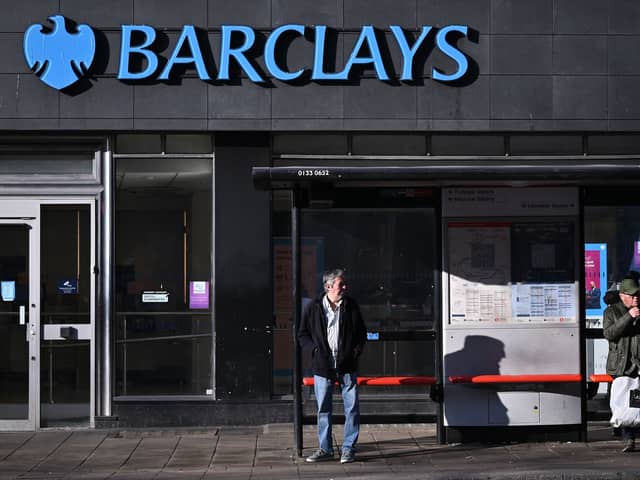Commuters wait at a bus stop outside a branch of Barclays in London.