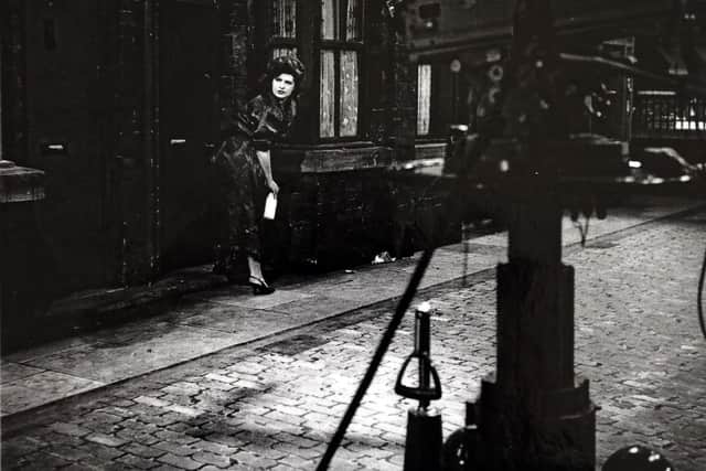 Elsie Tanner (Pat Phoenix) picks up a pint of milk from the Street with its painted cobbles