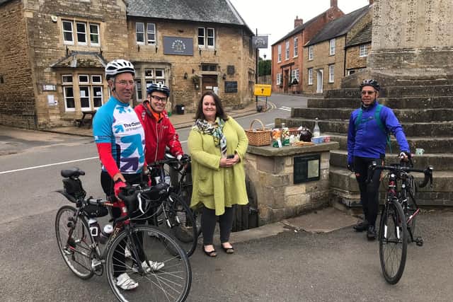 Challenge riders Keith Wright (left), Iain Dibble (centre) and Henry Laprun next to the cross in Geddington with Lisa Wilkinson from the village who provided some refreshments