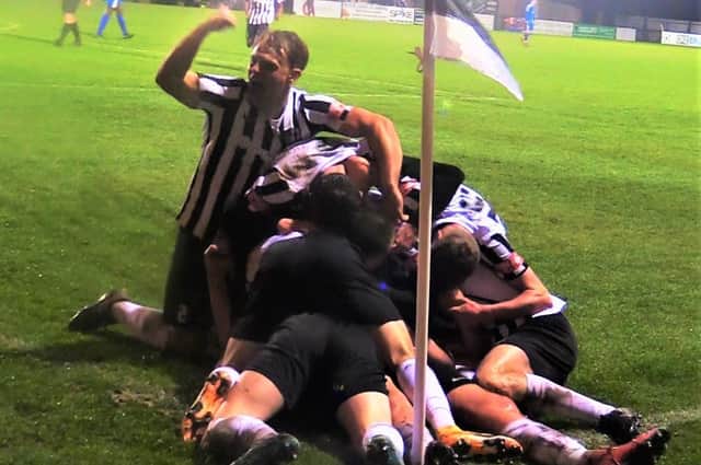 Lewis White is buried underneath a pile of his Corby Town team-mates after his second goal of the game deep into injury-time earned them a 2-1 victory over Sutton Coldfield Town at Steel Park. Picture by David Tilley