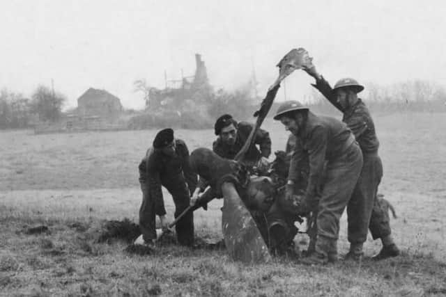 Members of the crash recovery crew struggle to move part of the destroyed aircraft’s engines and propeller. The remains of some of the buildings can be seen in the distance.