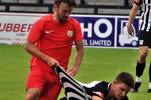 A Melton player gets hold of Jordan O'Brien, who scored twice in Corby's victory