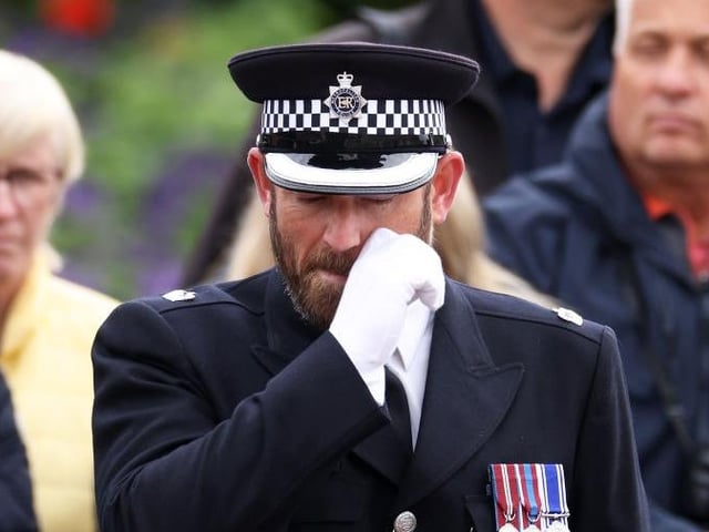 A police officer guarding the coffin's route wipes away a tear