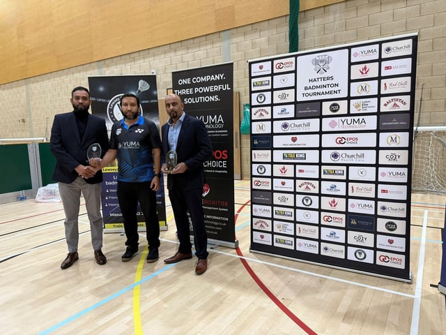 Tournament officials and sponsors pictured during the Hatters Badminton Tournament 2025, with sponsor boards displayed at the venue.