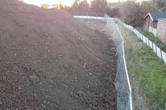 The pile of soil towers over the wire fence