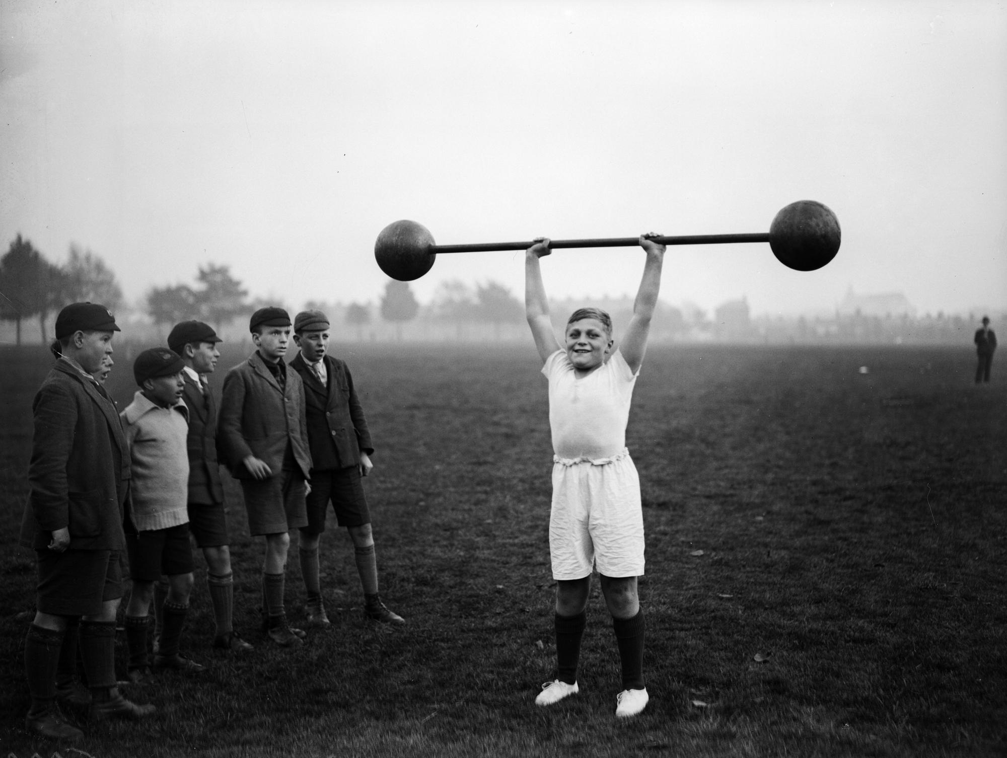 22nd October 1931:  Northampton schoolboy William Albert Tuckley raises a dumb-bell weighing 110 pounds above his head, to the amazement of his classmates. Eleven-year-old Tuckley is being trained by Mr French, weightlifting champion of Northamptonshire and Buckinghamshire.  (Photo by Fox Photos/Getty Images)