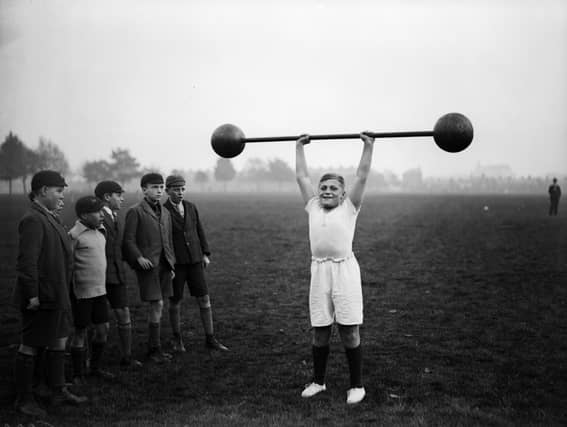 22nd October 1931: Northampton schoolboy William Albert Tuckley raises a dumb-bell weighing 110 pounds above his head, to the amazement of his classmates. Eleven-year-old Tuckley is being trained by Mr French, weightlifting champion of Northamptonshire and Buckinghamshire. (Photo by Fox Photos/Getty Images)