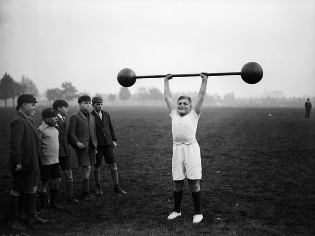 22nd October 1931:  Northampton schoolboy William Albert Tuckley raises a dumb-bell weighing 110 pounds above his head, to the amazement of his classmates. Eleven-year-old Tuckley is being trained by Mr French, weightlifting champion of Northamptonshire and Buckinghamshire.  (Photo by Fox Photos/Getty Images)