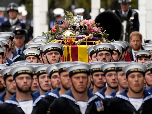 The coffin of Queen Elizabeth II with the Imperial State Crown resting on top surrounded by members of the Royal Navy is carried towards Westminster Abbey