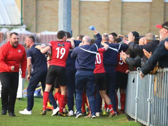 Aaron O'Connor is mobbed by players, staff and fans alike after his last-gasp goal gave Kettering Town a 1-0 win at Leiston and put them on the brink of the title. Pictures by Peter Short