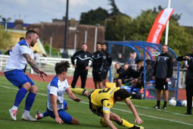 Sam Brown takes a tumble as he is challenged by two Enfield players
